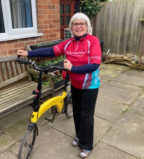 Sue stands next to her bicycle on her patio wearing a Cardiomyopathy cycling jersey.